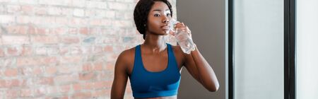 Panoramic orientation of african american sportswoman drinking water in living room
