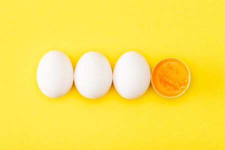 Top view of raw egg half among whole eggs on yellow backgroundの写真素材