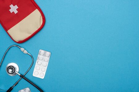 top view of pills in blister pack, stethoscope, first aid kit on blue background