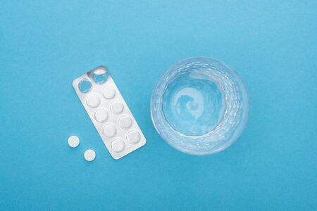 top view of pills in blister pack, glass of water on blue background