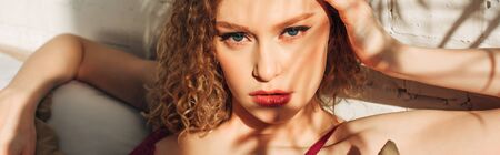 attractive sexy curly girl in red lingerie in bedroom with sunlight and shadows, horizontal concept