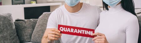 cropped view of ill couple in medical masks holding quarantine sign at home during self isolation,...