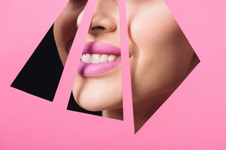 Cropped view of woman with pink lips smiling across triangular holes in paper on black backgroundの写真素材