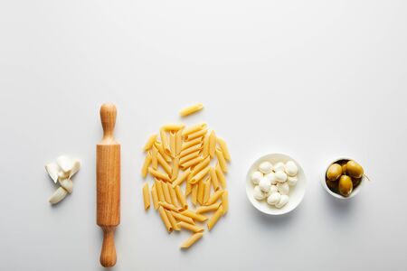 Flat lay with garlic, rolling pin, pasta and bowls with olives and mozzarella on white backgroundの写真素材