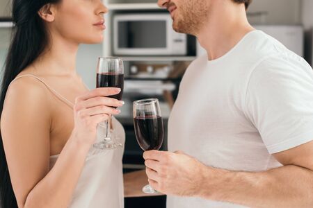 cropped view of couple holding glasses with red wine during self isolation at homeの写真素材