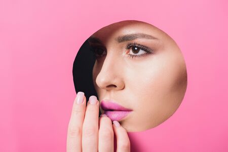 Attractive woman with pink lips looking across hole and touching paperの写真素材