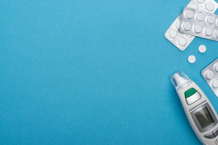 top view of pills in blister packs and infrared thermometer on blue background