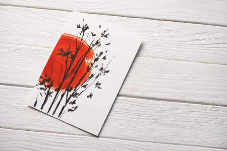 Top view of paper with Japanese painting with red sun and branches on wooden backgroundの写真素材