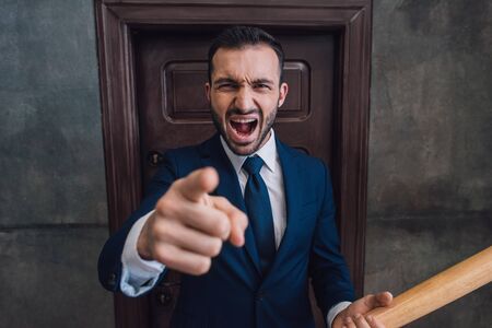 Selective focus of aggressive collector with baseball bat pointing with finger and shouting near...