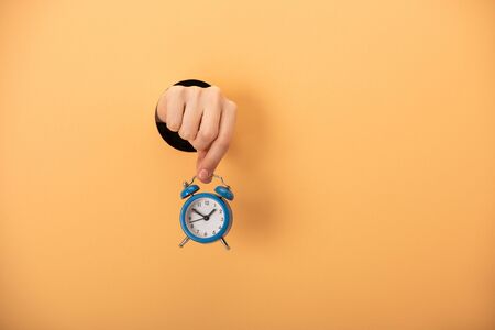 cropped view of woman holding alarm clock on orange
