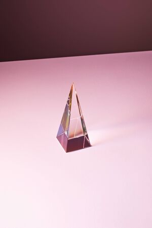 crystal transparent pyramid with light reflection on pink background