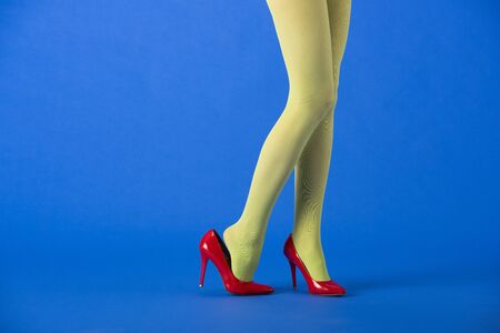 cropped view of stylish model in green tights and red heels posing on blueの写真素材