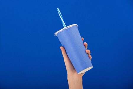 cropped view of woman holding paper cup with soft drink isolated on blueの写真素材