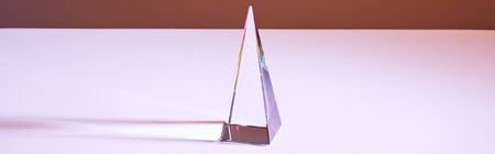 crystal transparent pyramid with light reflection on brown background, horizontal crop