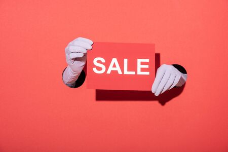 cropped view of woman in gloves holding paper with sale lettering on redの写真素材