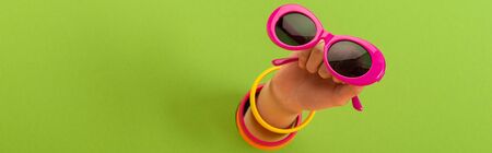 panoramic shot of woman holding pink sunglasses on greenの写真素材