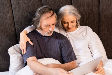 mature couple looking at laptop in bed at homeの写真素材