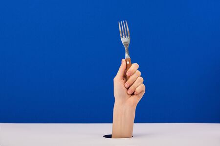 cropped view of woman holding stainless fork isolated on blue