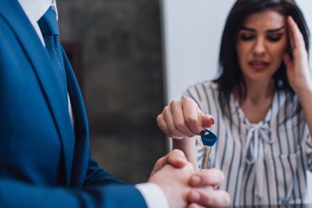 Selective focus of upset woman giving key to collector with clenched hands