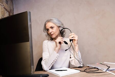 mature operator holding headset near computer monitor at homeの写真素材