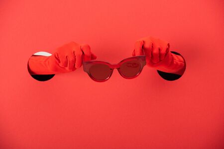 cropped view of woman in gloves holding trendy sunglasses on redの写真素材
