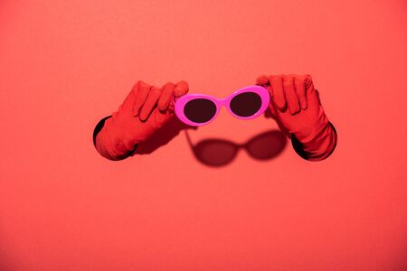 cropped view of woman in gloves holding pink sunglasses on redの写真素材