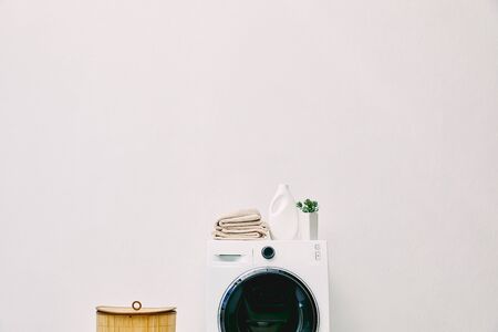 detergent bottle, towels and green plant on washing machine near laundry basket in bathroomの写真素材