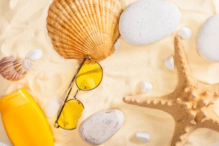 Top view of sunscreen and sunglasses near starfish and seashells on sandの写真素材