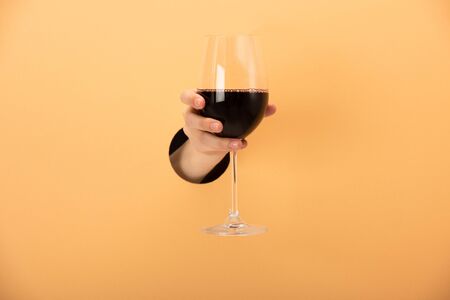 cropped view of woman holding glass of red wine on orangeの写真素材