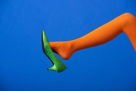 cropped view of woman in bright orange tights and green shoe on blue