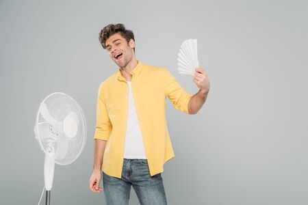 Excited man with electric and hand fans smiling and looking at camera isolated on greyの写真素材