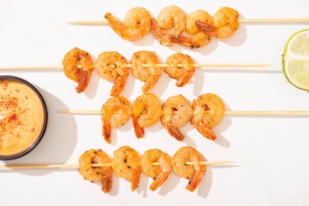 top view of delicious fried prawns on skewers with lime and sauce on white backgroundの写真素材