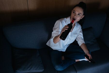 high angel view of depressed woman drinking wine from bottle while sitting on sofaの写真素材