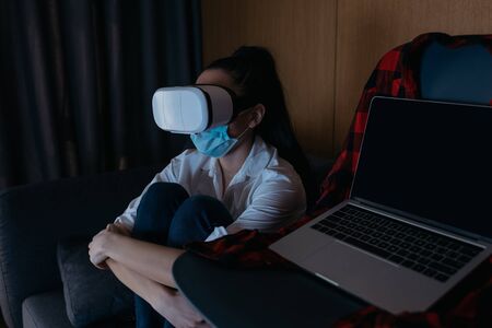 depressed woman sitting on sofa in vr headset near laptop with blank screen on chairの写真素材