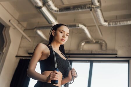 Low angle view of beautiful sportswoman with skipping rope looking at camera in gym