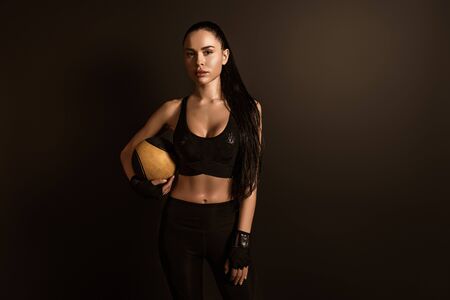 Brunette sportswoman with ball looking at camera isolated on blackの写真素材
