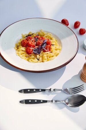 delicious pasta with tomatoes served with cutlery on white table in sunlight