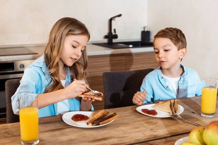selective focus of kid making toast with jam near brother at homeの写真素材