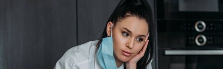 horizontal image of pensive young woman with medical mask hanging on earの写真素材