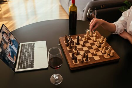 cropped view of woman playing chess during video call with boyfriend near red wine on tableの写真素材