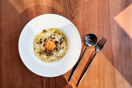 top view of delicious pasta carbonara served with black cutlery on wooden background in sunlightの写真素材