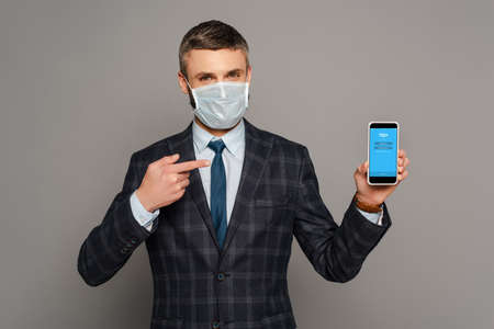 KYIV, UKRAINE - MARCH 30, 2020: handsome businessman in medical mask pointing with finger at...