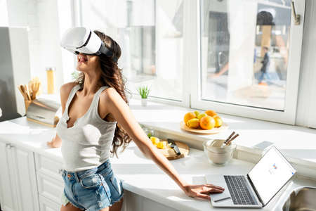 KYIV, UKRAINE - MARCH 13, 2020: Young woman using vr headset near laptop with google website and credit card in kitchenのeditorial素材
