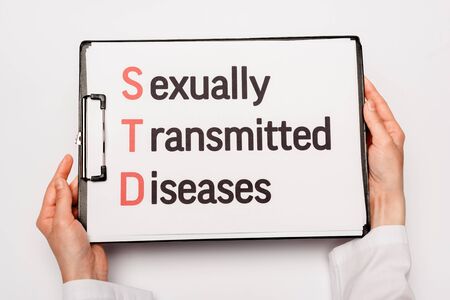cropped view of doctor holding clipboard with sexually transmitted diseases lettering isolated on whiteの写真素材