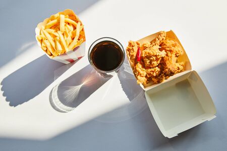 top view of tasty deep fried chicken, french fries and soda in glass on white table in sunlightの写真素材