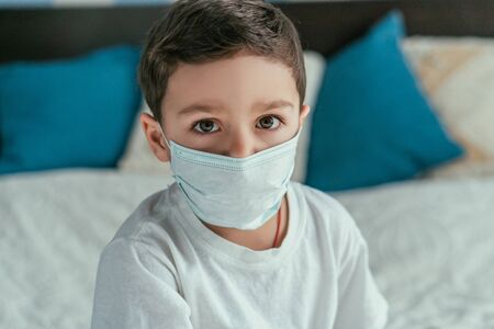 cute toddler boy in medical mask looking at camera at homeの写真素材