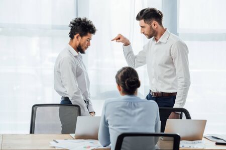 Selective focus of businessman pointing with finger at offended african american colleague in officeの写真素材