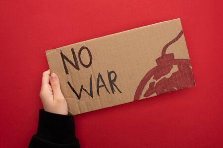 cropped view of woman holding cardboard placard with no war lettering and bomb on red backgroundの写真素材