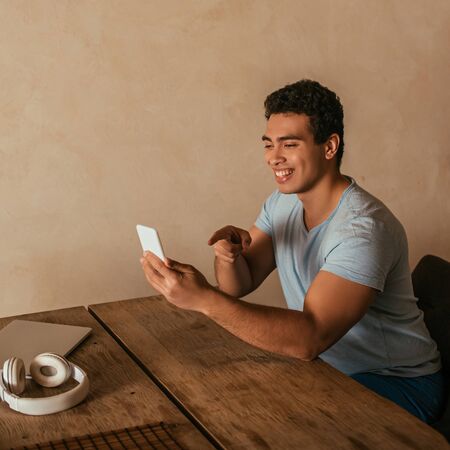 happy mixed race man pointing and having video call on smartphone at home on quarantine