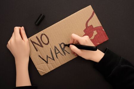 cropped view of woman drawing placard with no war lettering and bomb on black backgroundの写真素材